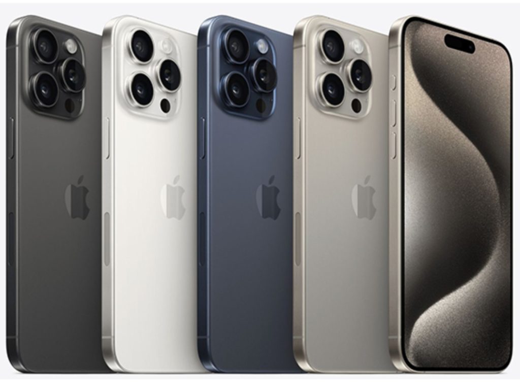 Four iPhone 15 Pro Max smartphones arranged in a row, showing the back design with quad-camera setups in four colors: a dark Black on the far left, a bright White, a deep Blue, and a light grey Titanium on the far right.